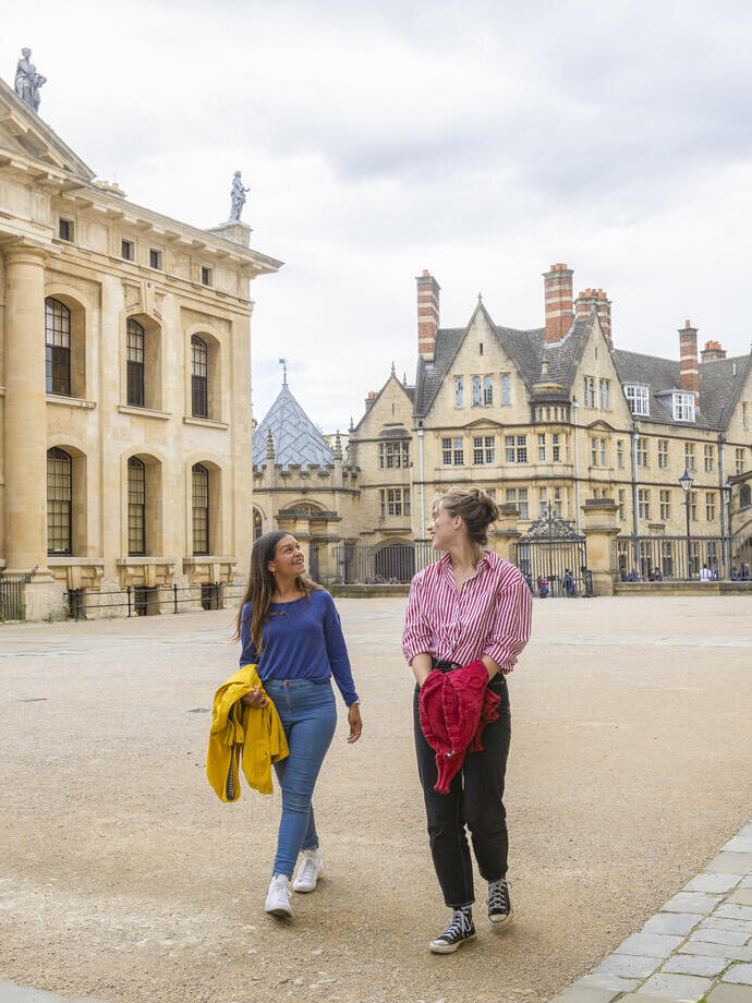 Two women walk across a courtyard among heritage buildings