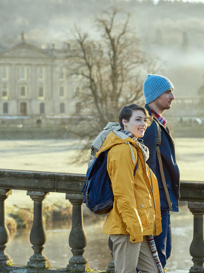 Couple walking on a stone bridge, a large country house in the backround