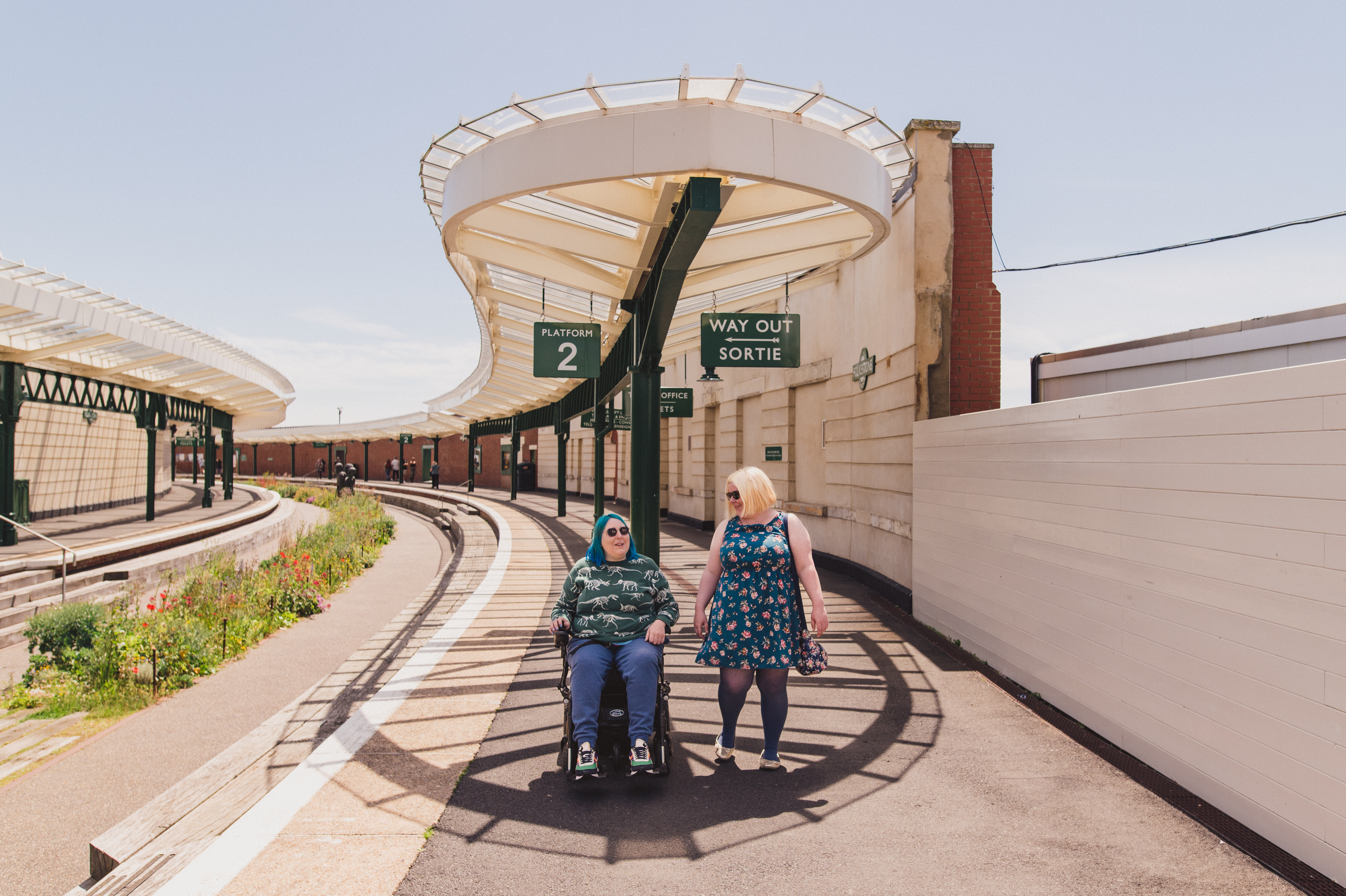Una donna cammina con un'altra donna seduta su una sedia a rotelle in una vecchia stazione ferroviaria.