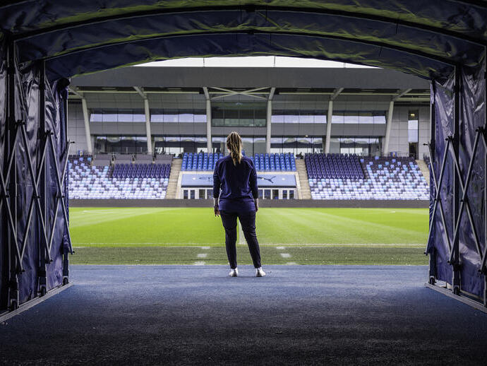 Frau, die vor dem Spielfeld im Manchester City Academy Stadium steht