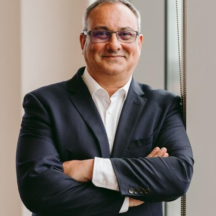A person in a suit standing with arms crossed near a window.
