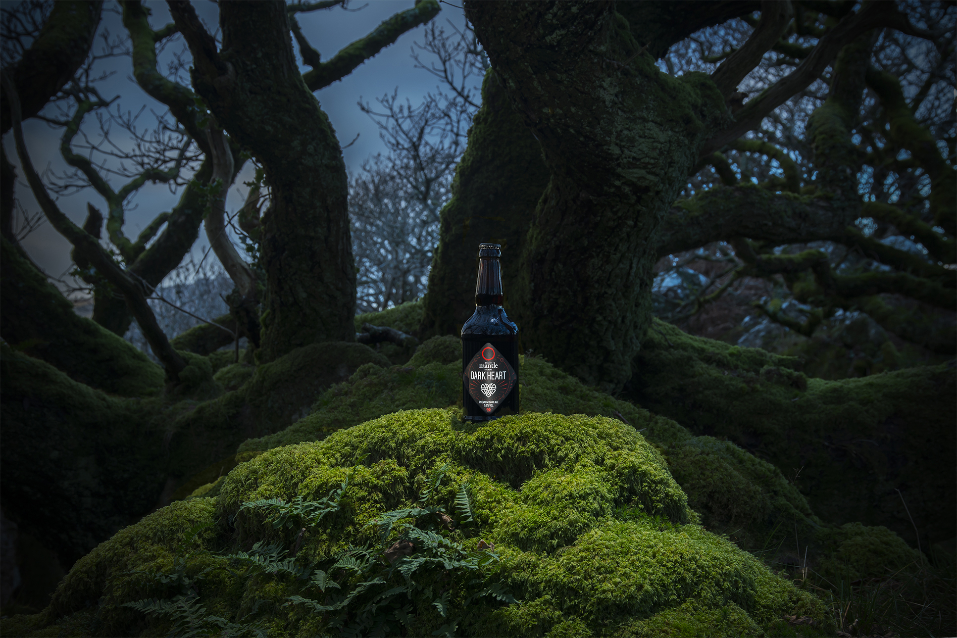A bottle of alcohol posed in front of some trees at night at Mantle Brewery