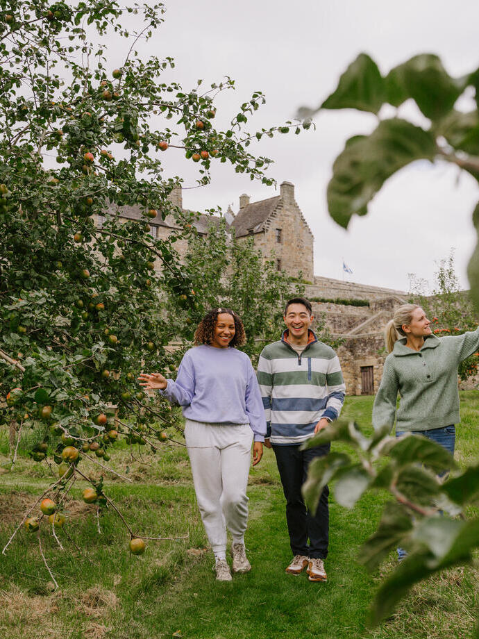 A man and two women walking through an apple orchard on castle grounds.