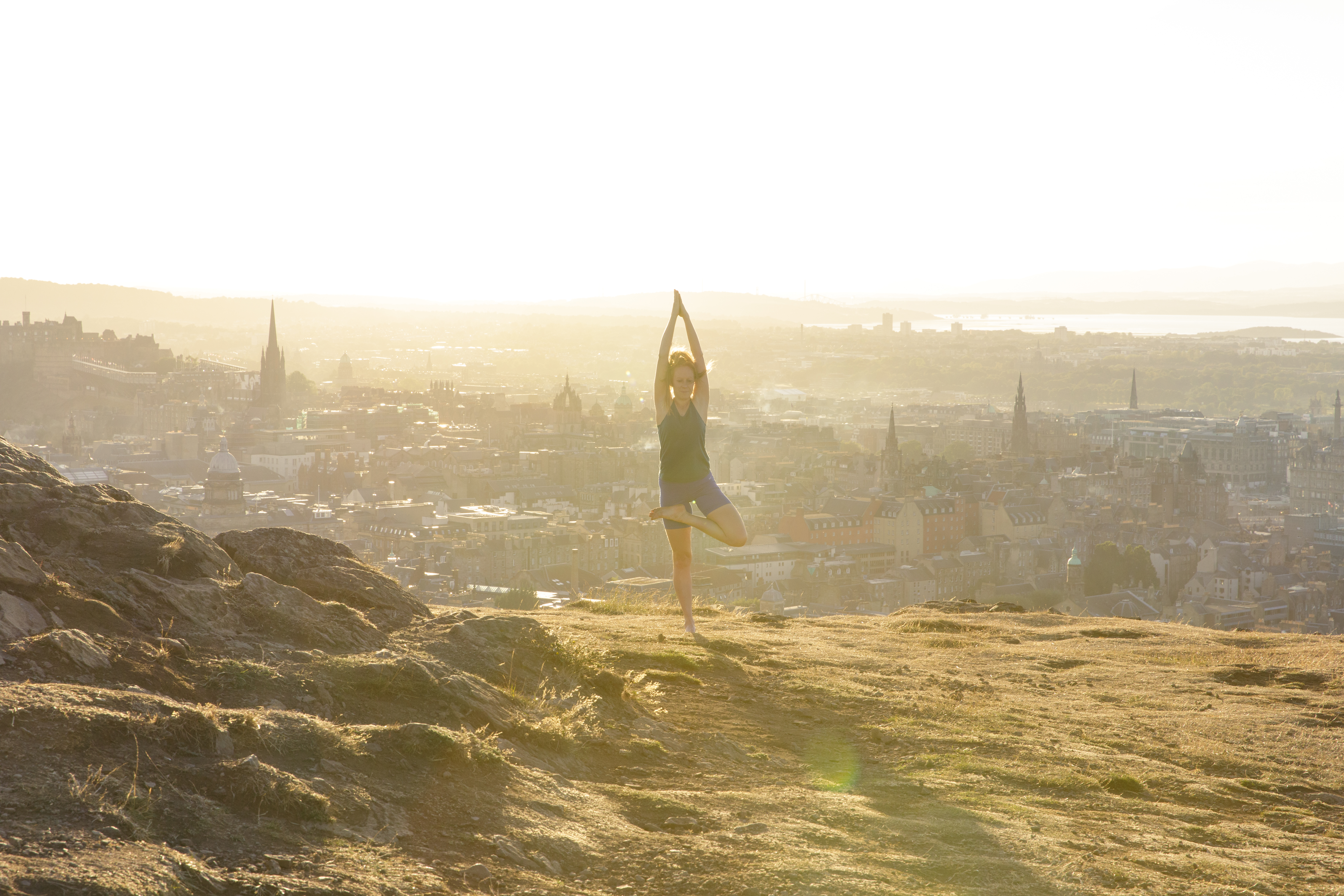 Young woman doing yoga on a hill overlooking a city