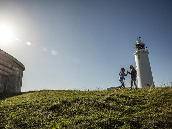 Two children playing in open space by a lighthouse
