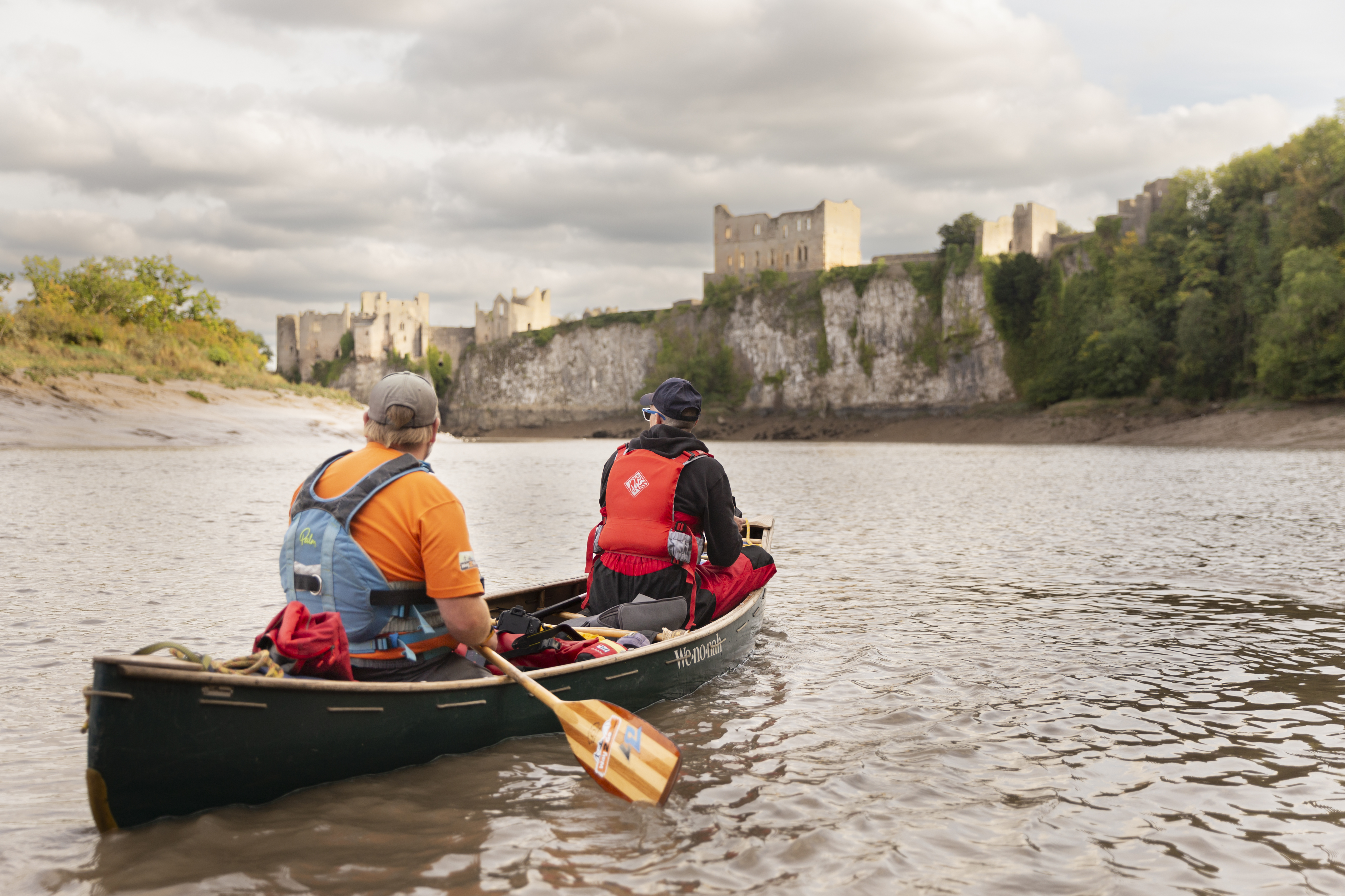 Two people rowing a boat on a river towards Chepstow Castle