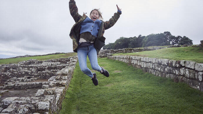 Girl leaping into the air with raised arms near stone wall