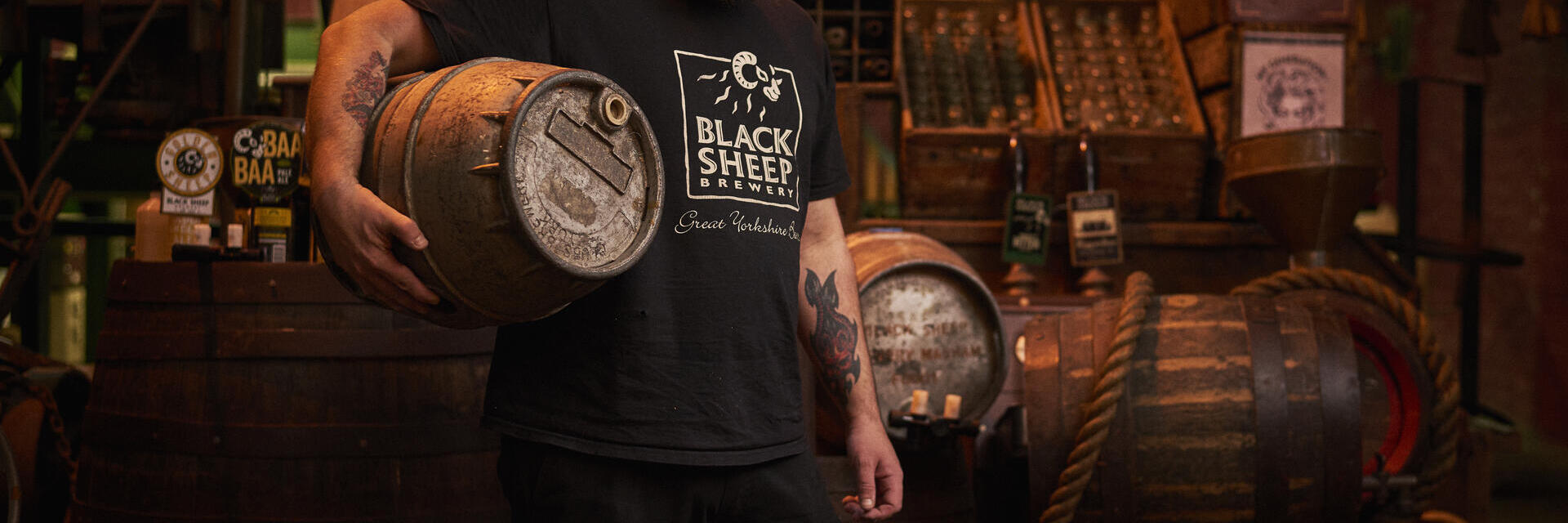 Uomo in piedi in un magazzino, con in mano un barile di birra in legno