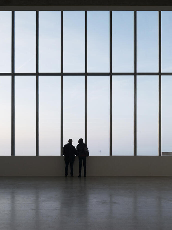Two silhouetted people staring out of a wide window in a contemporary building