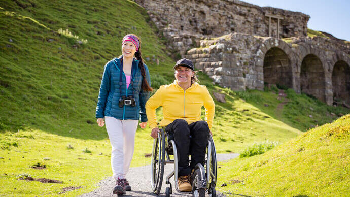 Man and woman at the top of a hill and the man is using a wheelchair and binoculars