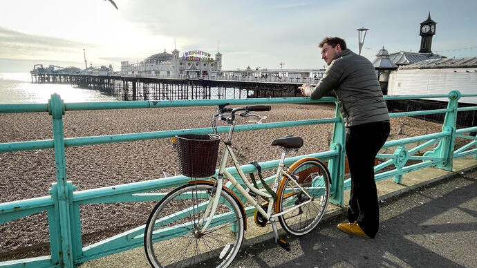Mann, der mit einem Fahrrad an einem Geländer am Meer lehnt