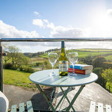 View from the balcony with a bistro table and chairs set with two novels, two wine glasses and a bottle of wine with a rural landscape in the background.