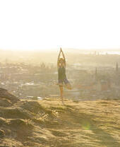 Una joven haciendo yoga en una colina con vistas a la ciudad