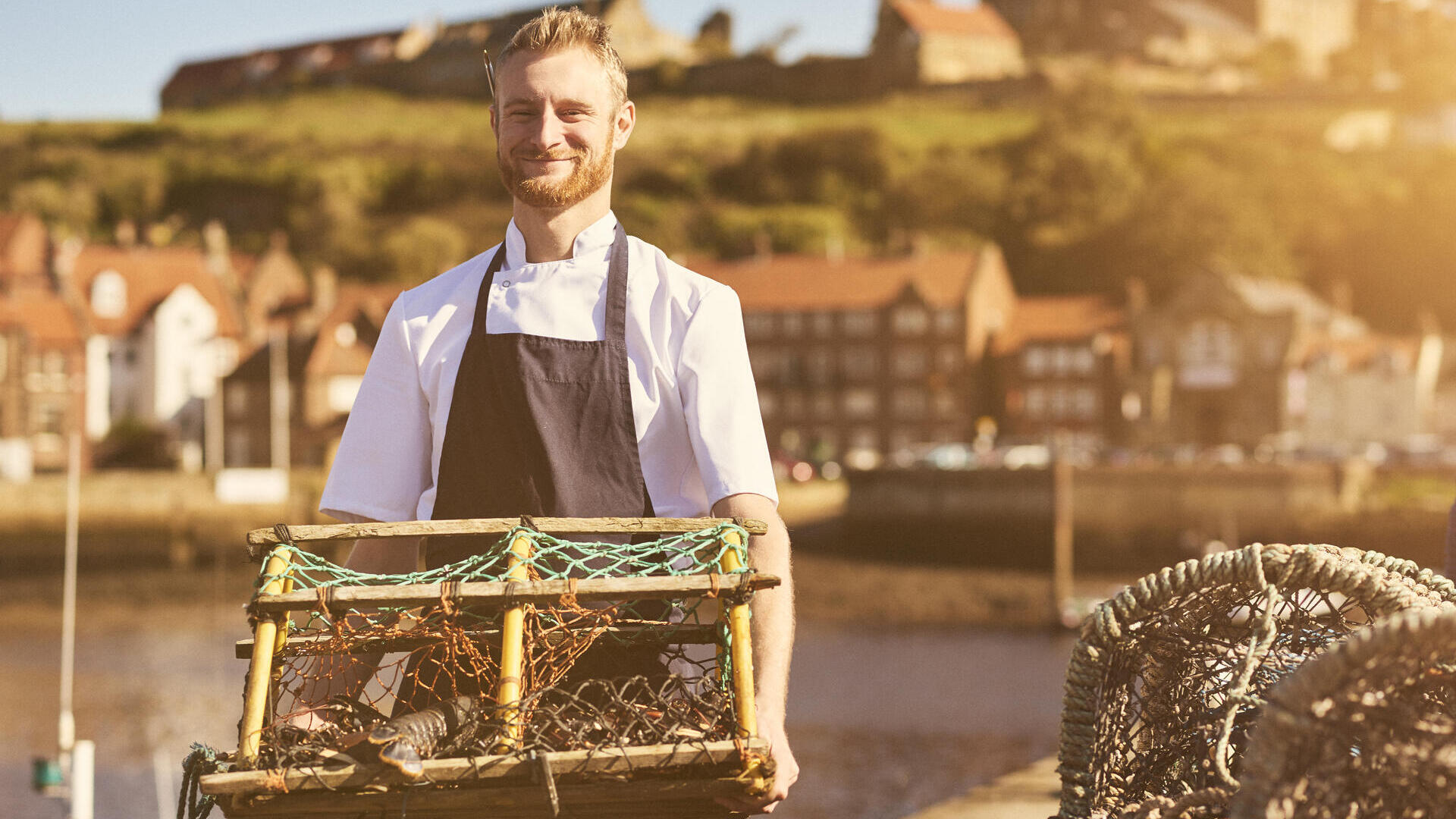 Man holding a lobster trap on a pier in the sunshine