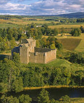 Exterior of a partly ruined medieval castle on a small hilltop overlooking fields and trees in autumn.