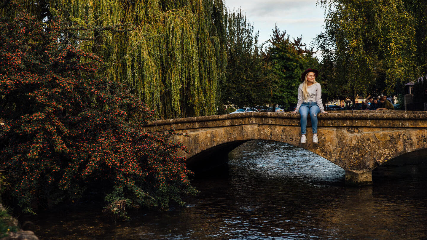 Frau, die auf einer niedrigen Brücke über einem Fluss in einem Dorf sitzt