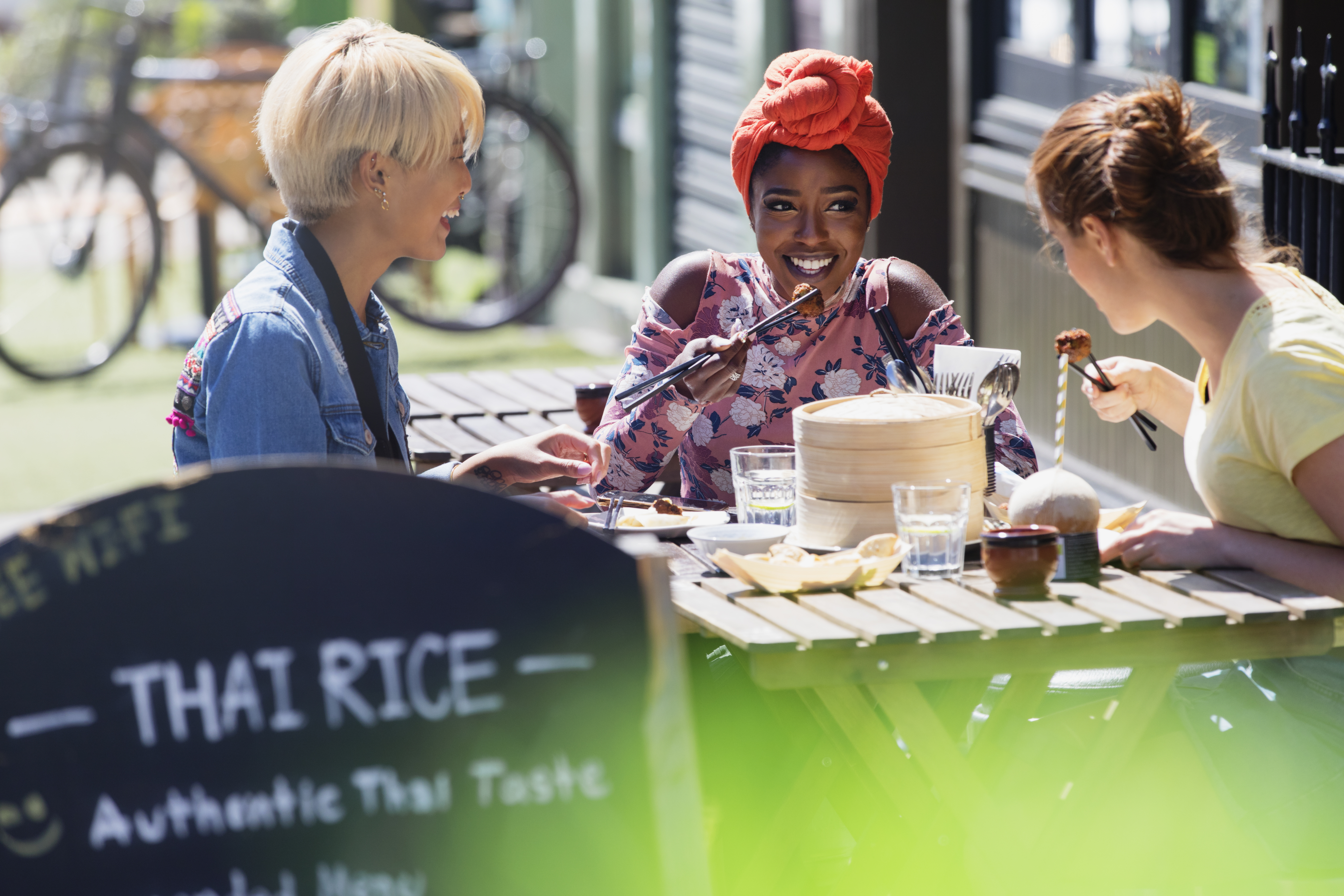 Drei junge Freundinnen genießen ein Dim-Sum-Mittagessen in einem sonnigen Straßencafé