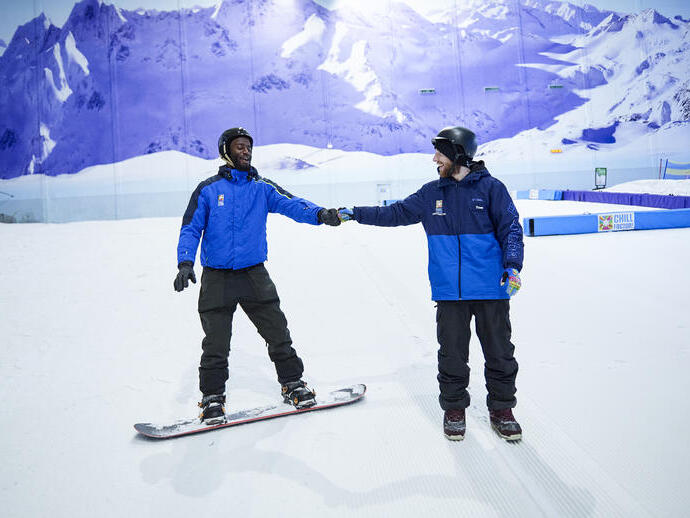 Two men skiing and snowboarding on an indoor snowslope at Chill Factore in Manchester