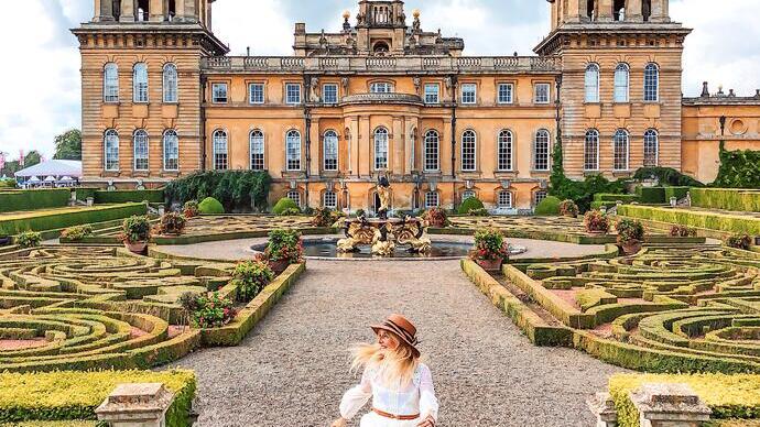 Mujer caminando por los jardines formales frente a un palacio