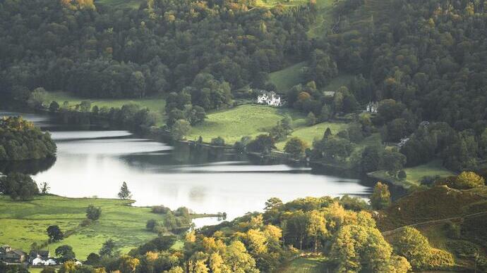 Two people sat on the edge of a fell looking over a green valley with a lake at the bottom