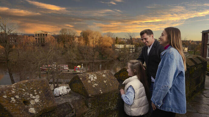 A family of three look out over a town river from a bridge.