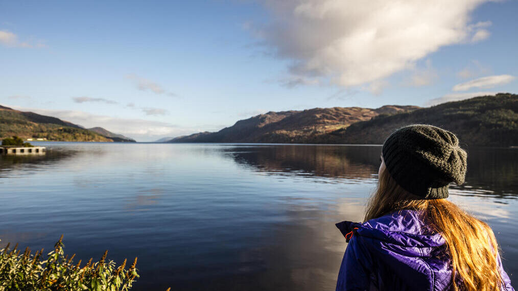 Femme debout au bord d'un lac entouré de collines