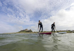 Two men on are paddleboarding in the sea with a heritage castle in the background.