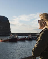 A woman, wearing sunglasses, looking out from the harbour