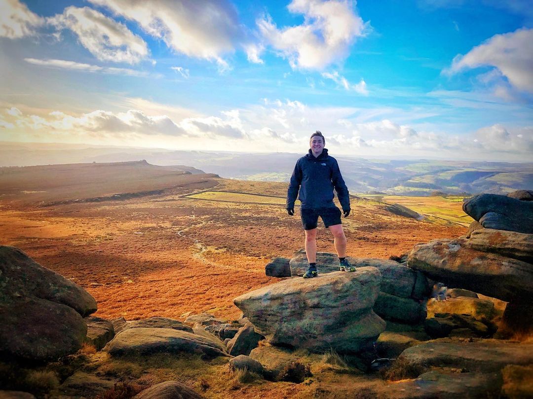 Ein Mann posiert auf dem Gipfel des Higger Tor mit weitem Blick auf den Peak District im Hintergrund