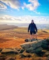 A man posing on top of Higger Tor with a wide view of the Peak District behind