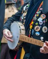 A folk player covered in badges at a music festival.