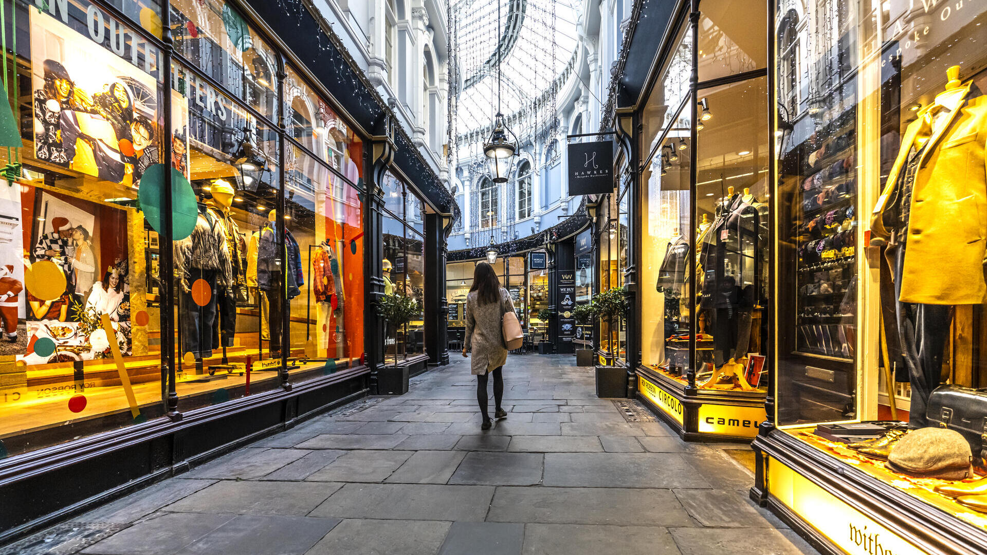 Mujer caminando por una galería entre tiendas, iluminada desde el interior