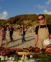 Un uomo in posa dietro una fila di cibi cotti al barbecue al Taste of Scilly Food Festival sull'isola di Tresco