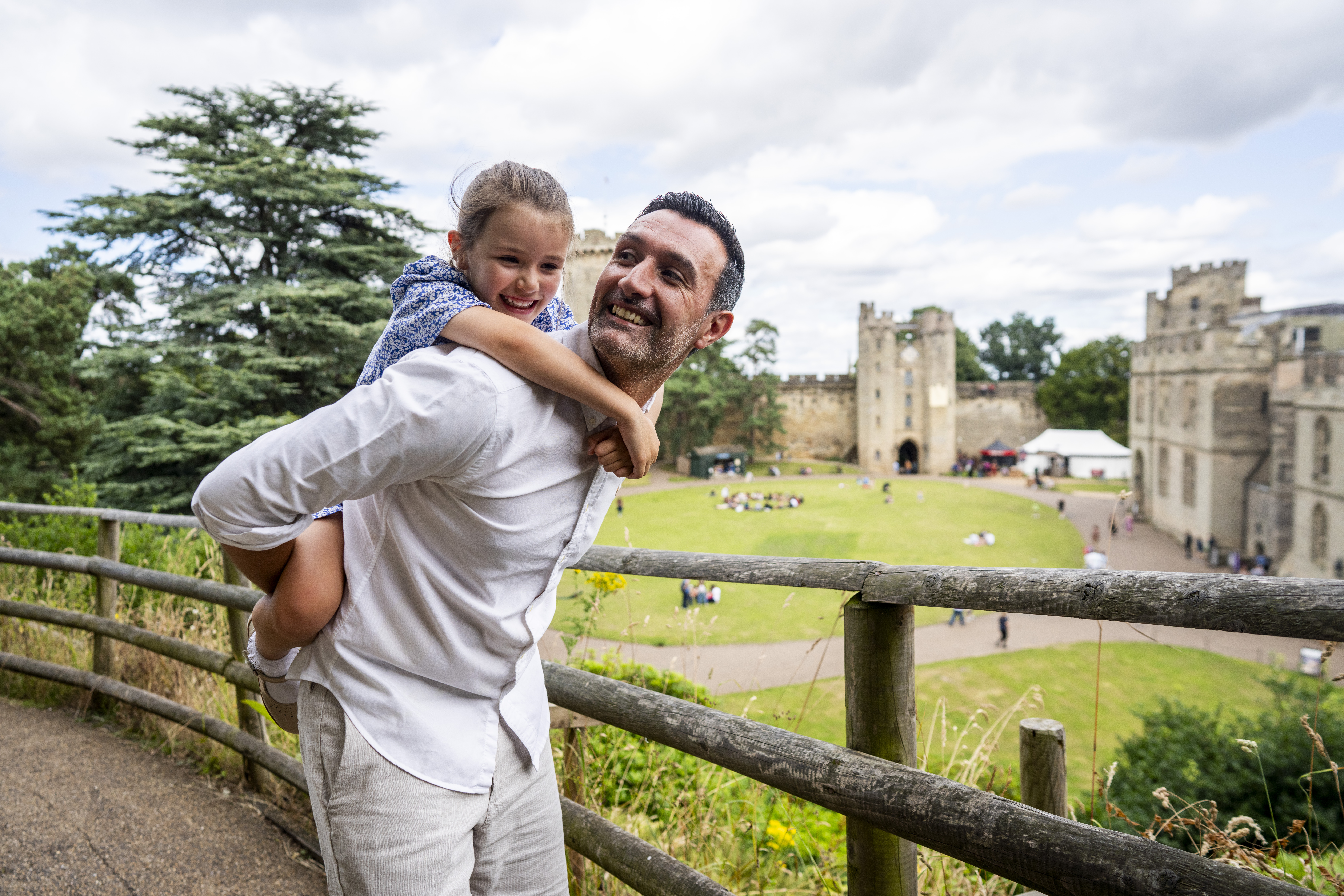 A man holds his daughter on his back in front of a heritage castle