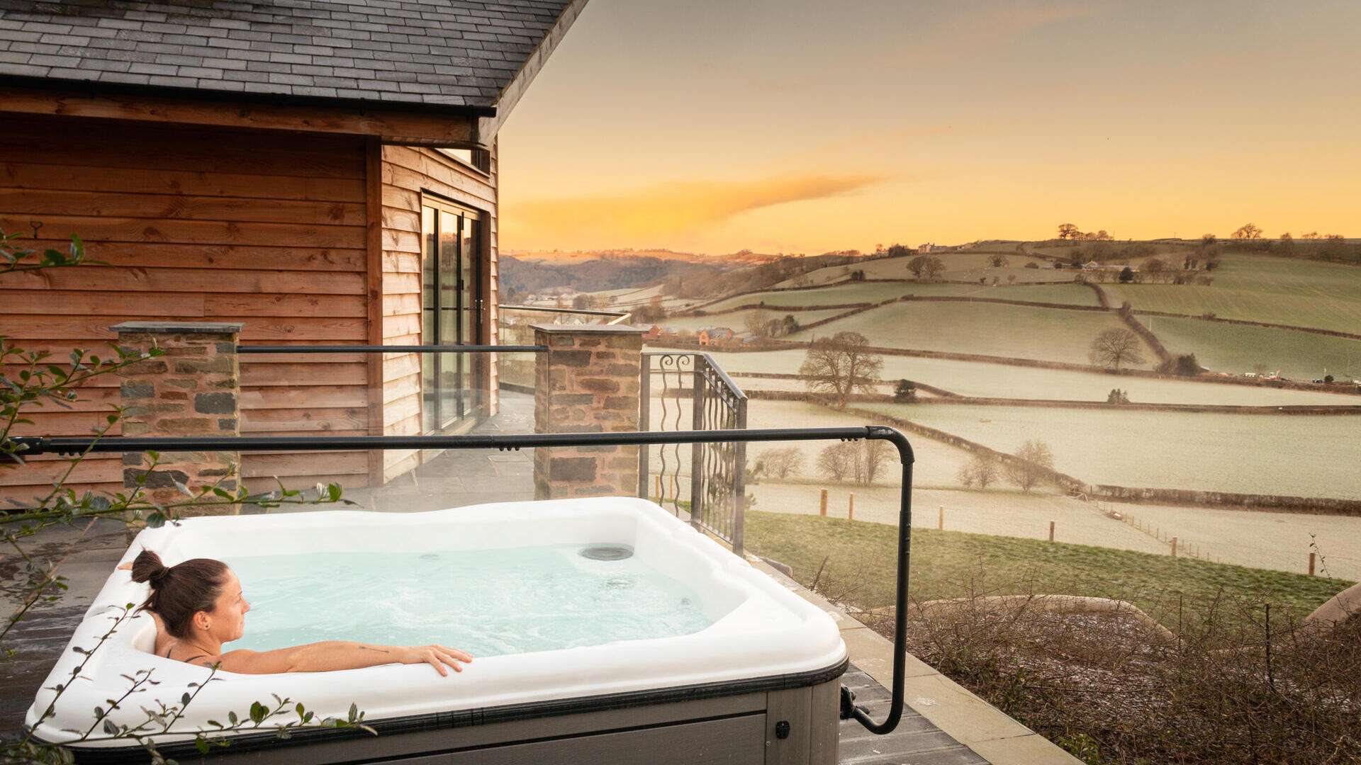 A woman in an outdoor Hot Tub,looking out across rolling farmland in the morning mist.