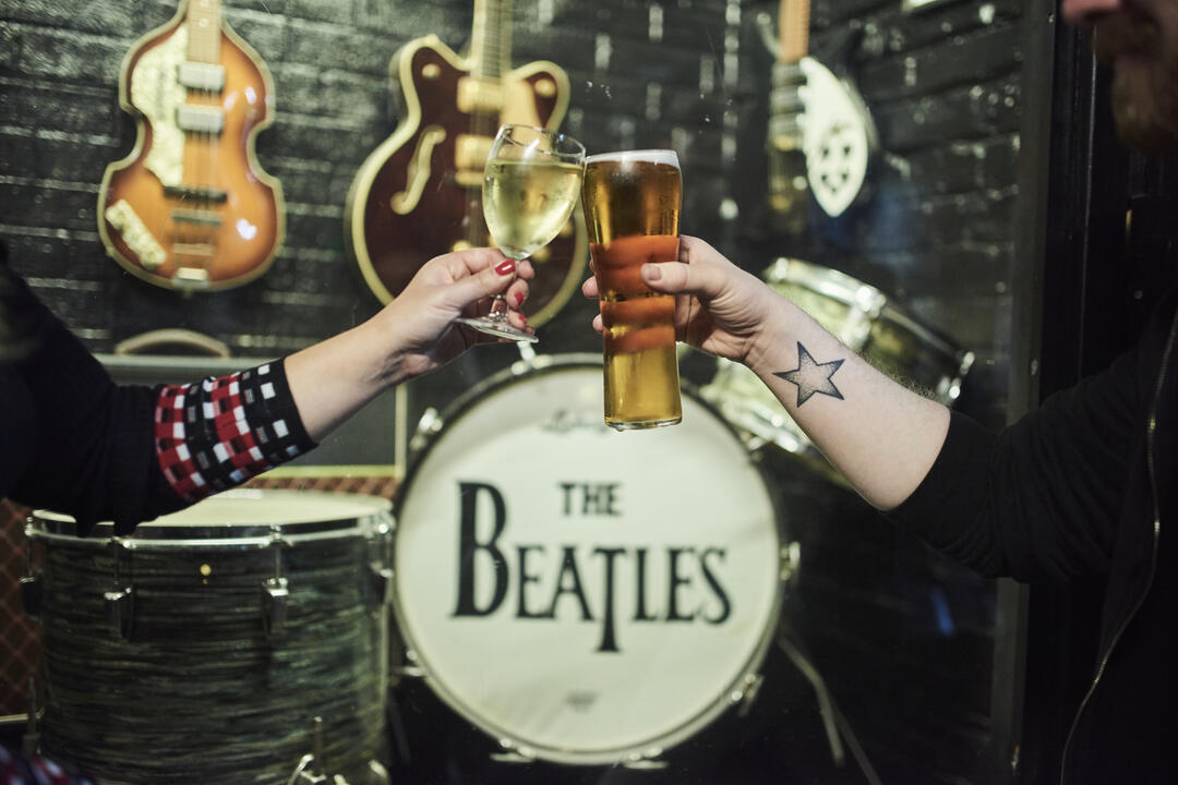 Two people clinking glasses in front of a drum kit and guitars
