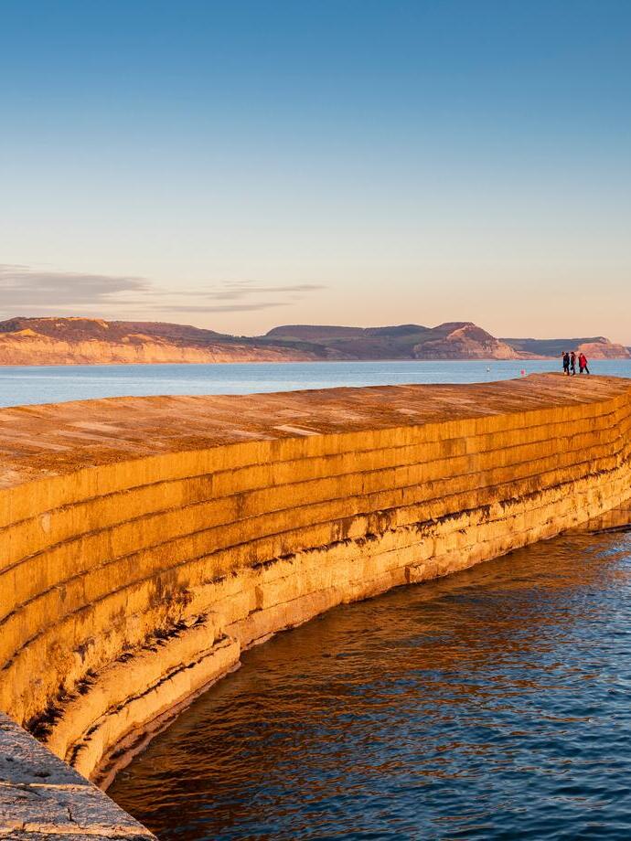 People at the end of the cobb overlooking the ocean at sunset
