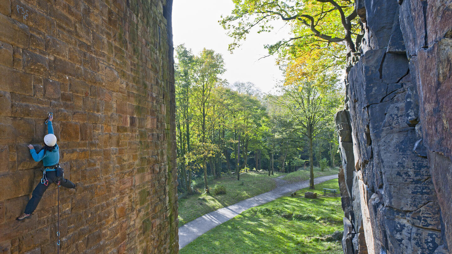 A climber using climbing gear scaling the underside of the arch of a bridge