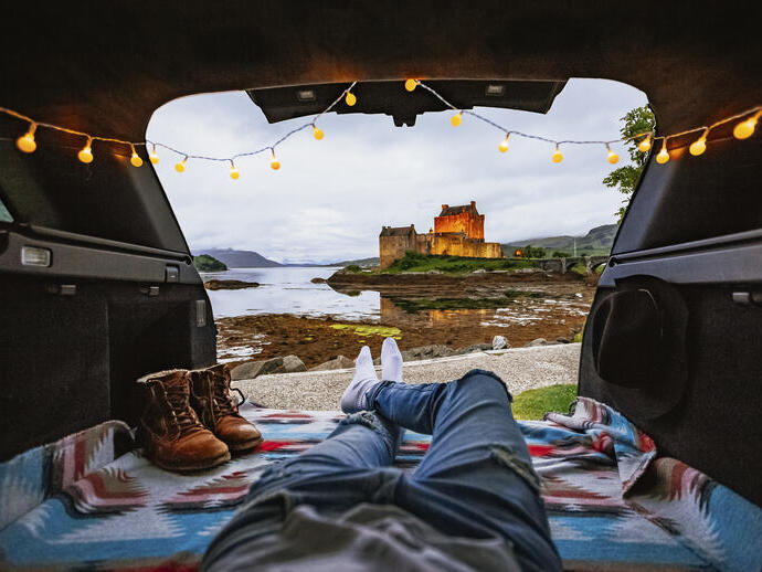 Mann liegt in einem Wohnmobil und schaut auf eine Burg in der Ferne