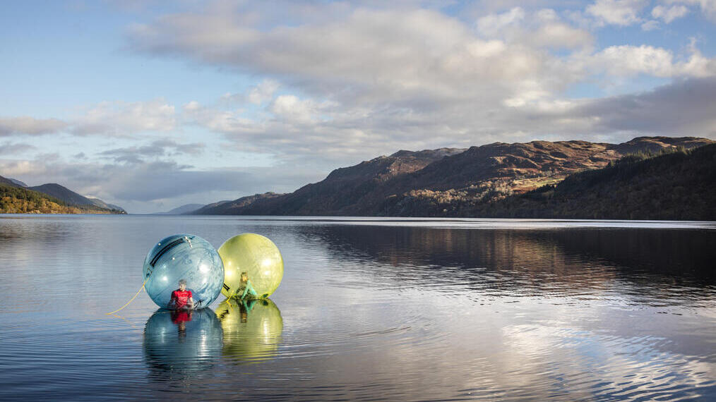 Menschen beim Zorbing auf einem von Bergen umgebenen See