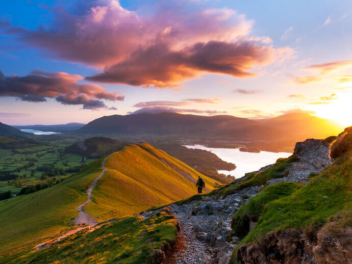 Hiker walking along a path on a mountain ridge at sunrise