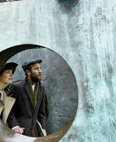 Couple vu à travers une ouverture dans une grande sculpture en bronze dans un jardin