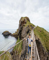 Child crossing a long rope bridge over the cliffs by the sea