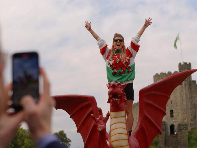 Woman standing with arms outstretched on a model Welsh dragon in front of a castle