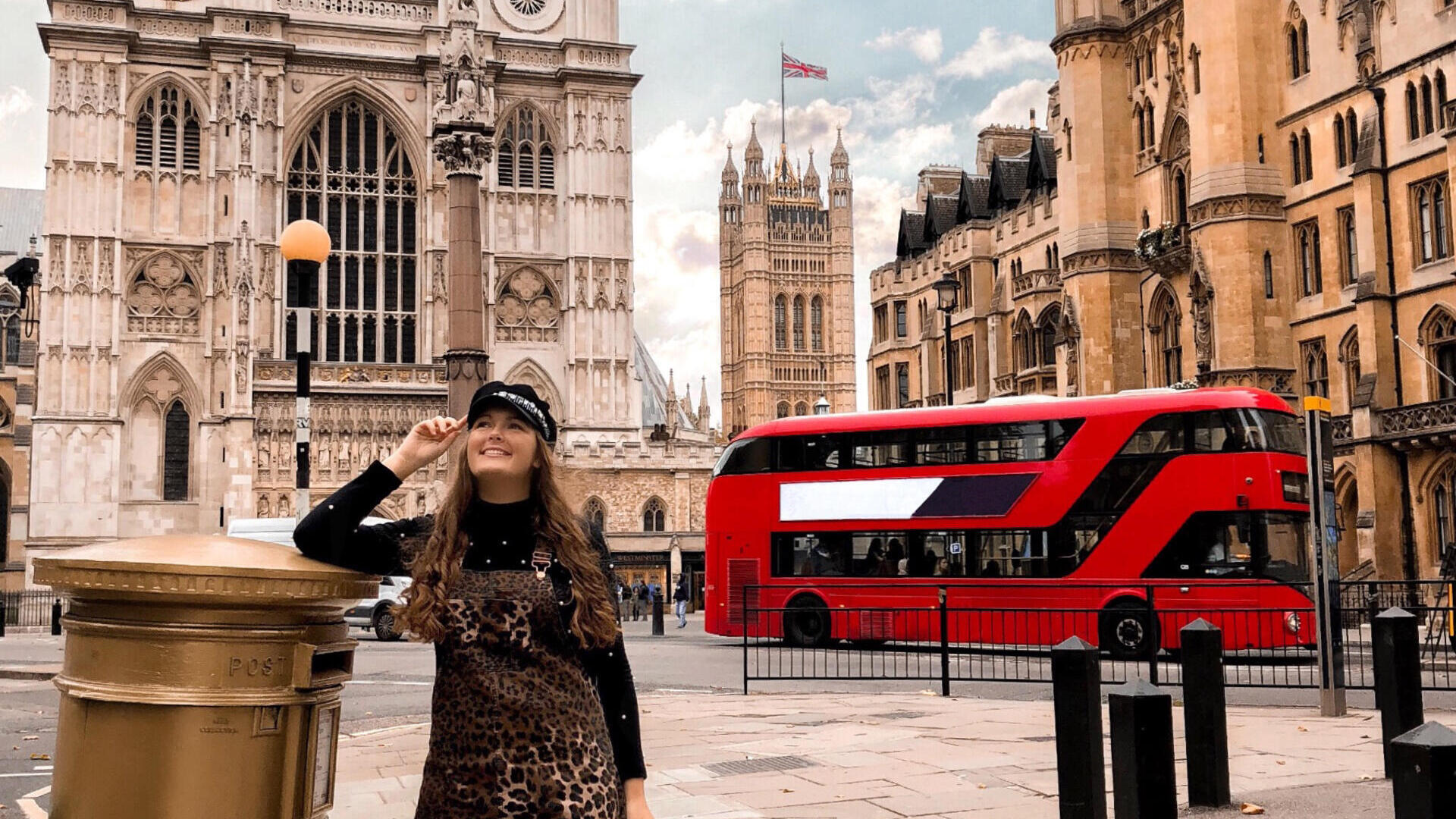 Woman standing by a golden letter box and a red bus behind
