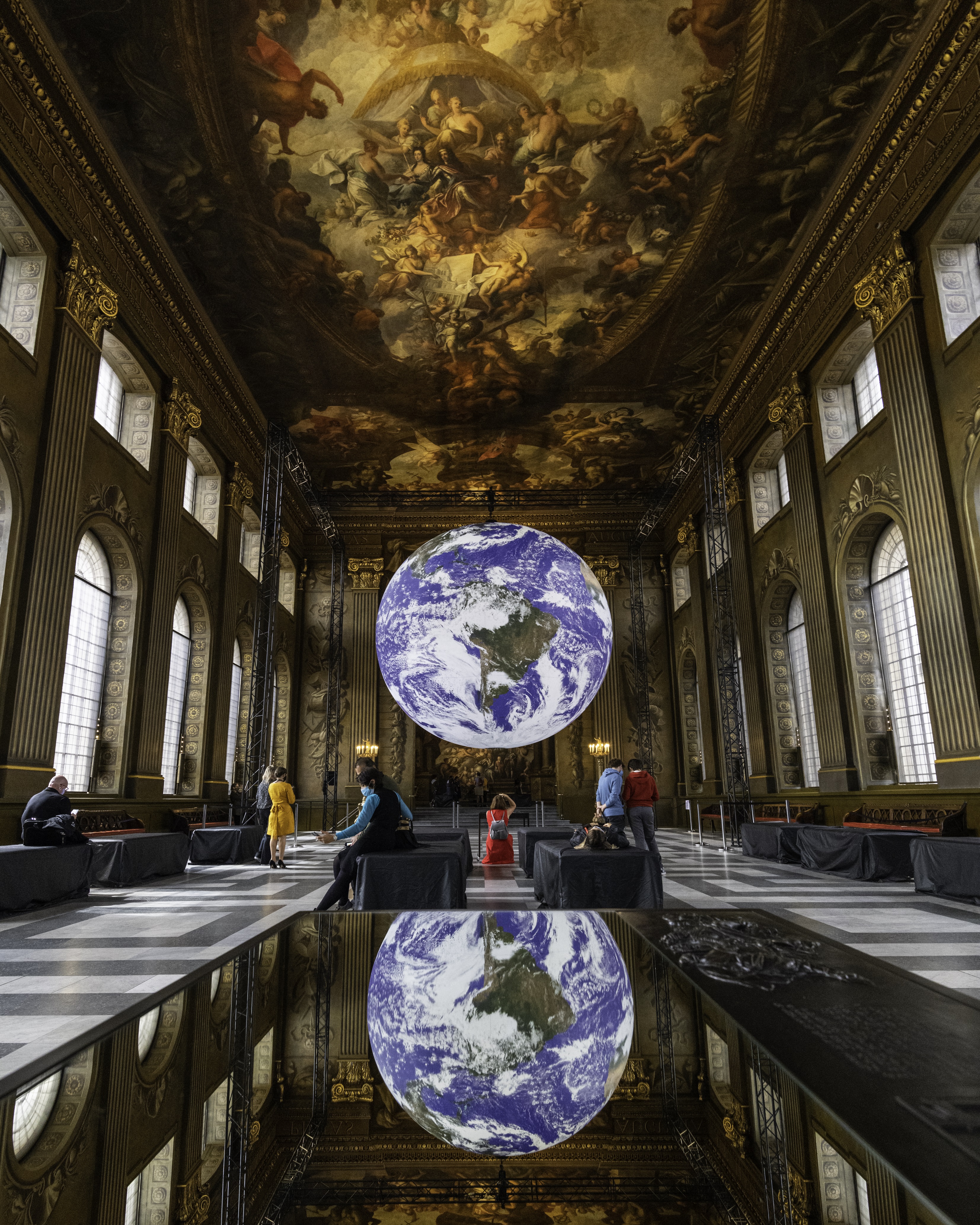People in a large hall in which a sculpture of an illuminated planet Earth hangs from the ceiling