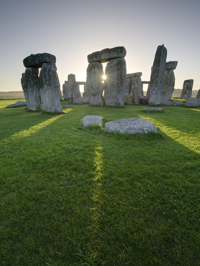 Large stone pillars arranged in circle on grass. Sunset