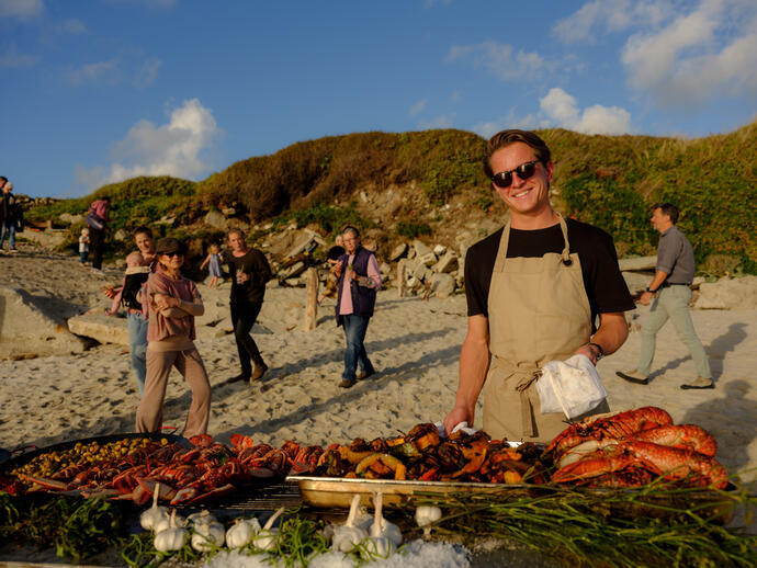 Un hombre posando detrás de una fila de comida a la barbacoa en el Taste of Scilly Food Festival en la isla de Tresco