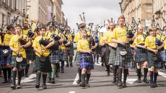 Una banda di bambini in kilt e magliette gialle suona la cornamusa mentre marcia per le strade.