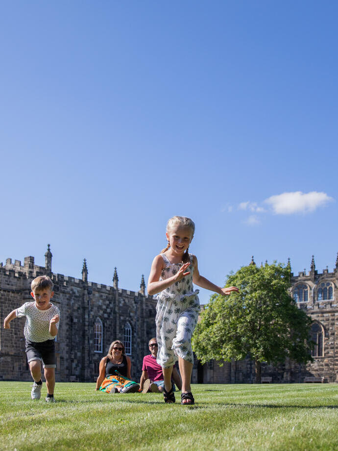 A family running across a lawn in front of a historical building in Durham